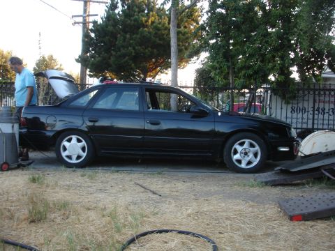 1991 Ford Taurus - Side view of a black 1991 Ford Taurus sedan parked outdoors with its trunk open.