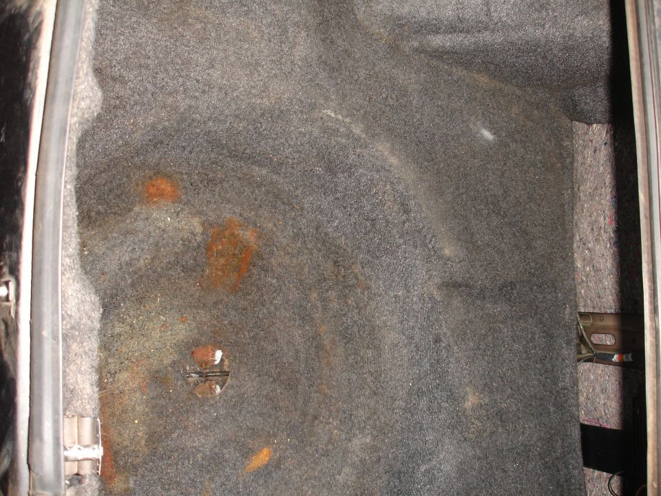 Sedan trunk floor with gray carpet and rust-brown moisture staining