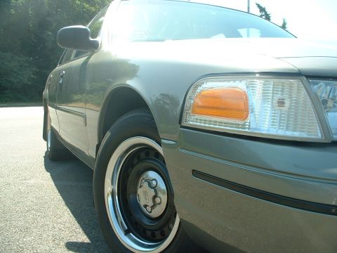 2000 Ford Crown Victoria - A gray 2000 Ford Crown Victoria is shown from the front quarter angle, highlighting its wheel and headlight assembly.