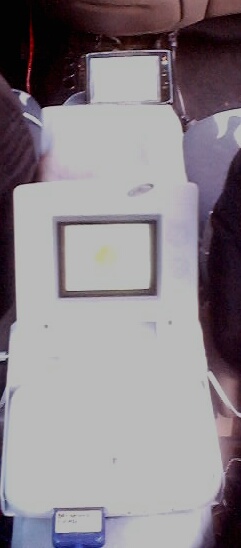 1999 Ford Taurus - Out-of-focus photo of a white box-shaped device with a small recessed screen, held or mounted inside a vehicle cabin.