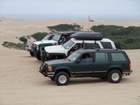 1985 Toyota 4Runner - Several off-road vehicles are lined up on sand dunes near the ocean.