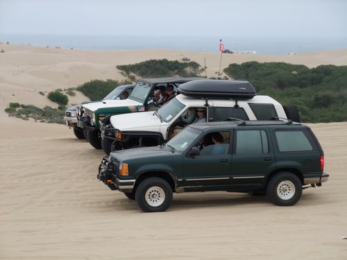 Dark green Ford Explorer with winch bumper and two other 4x4s on coastal sand dunes