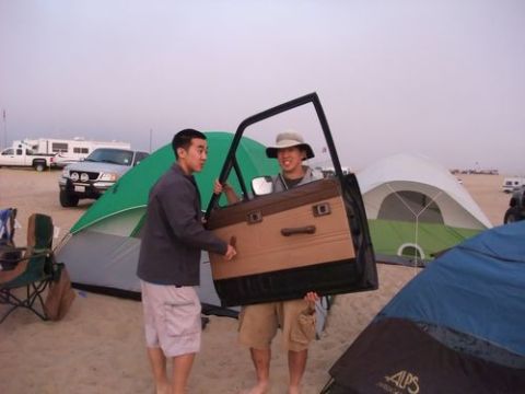 1985 Toyota 4Runner - Two men are holding a car door while camping on the beach with tents and RVs in the background.