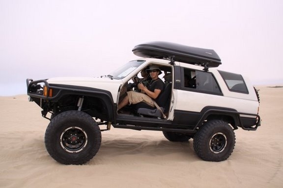 Lifted white Toyota 4Runner with doors off and roof box on sand dunes