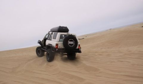 1985 Toyota 4Runner - A white SUV navigates sandy terrain, kicking up dust as it drives up a dune.