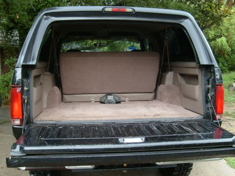 1992 Ford Bronco - The cargo area of a black Ford Bronco is visible with the tailgate open, revealing the folded rear seat and carpeting.