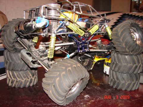 1987 Ford Bronco - RC monster truck chassis with large tires and yellow shocks is shown up close.