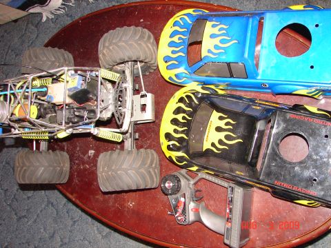 1987 Ford Bronco - A remote control monster truck chassis and two flame-decorated bodies are laid out on a table with a controller.