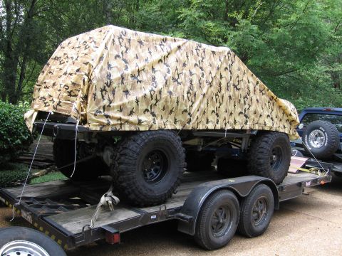 1967 Ford Mustang - A vehicle covered in a camouflage tarp is transported on a trailer, with another vehicle visible in the background.