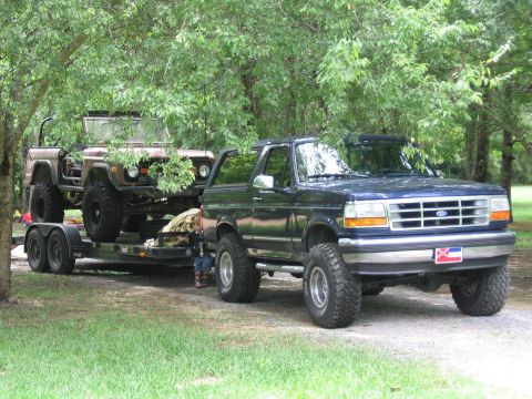 1967 Ford Mustang - A dark blue Ford Bronco is parked on the right, towing a trailer with a brown Ford Bronco loaded on it.