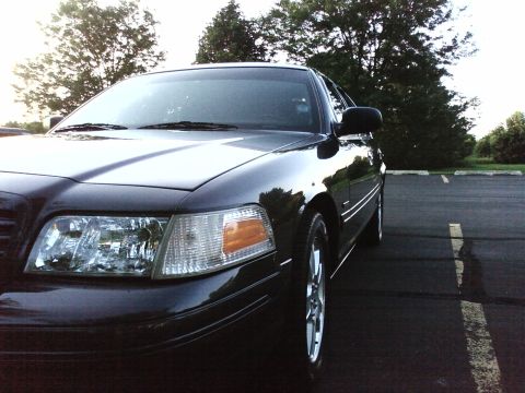 2004 Ford Crown Victoria - A black 2004 Ford Crown Victoria is parked in a lot, showing its front quarter panel and headlight.