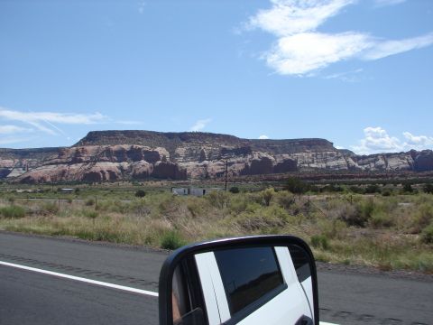 1992 Ford Taurus - A scenic view of layered rock formations under a blue sky with scattered clouds, seen from a moving vehicle.