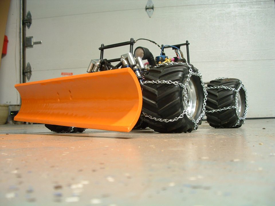 RC monster truck with orange snow plow and chained tires on garage floor