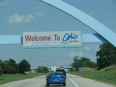 1992 Ford Taurus - A blue car drives on a highway under a large sign welcoming travelers to Ohio.
