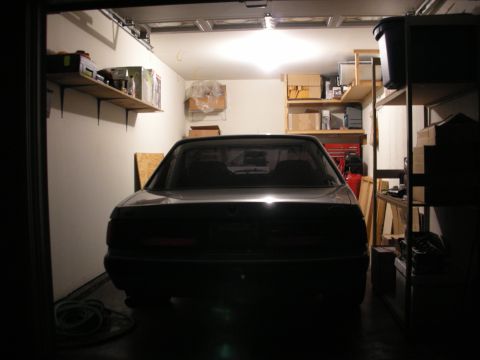 1990 Ford Mustang - The rear of a dark sedan is visible inside a cluttered garage.