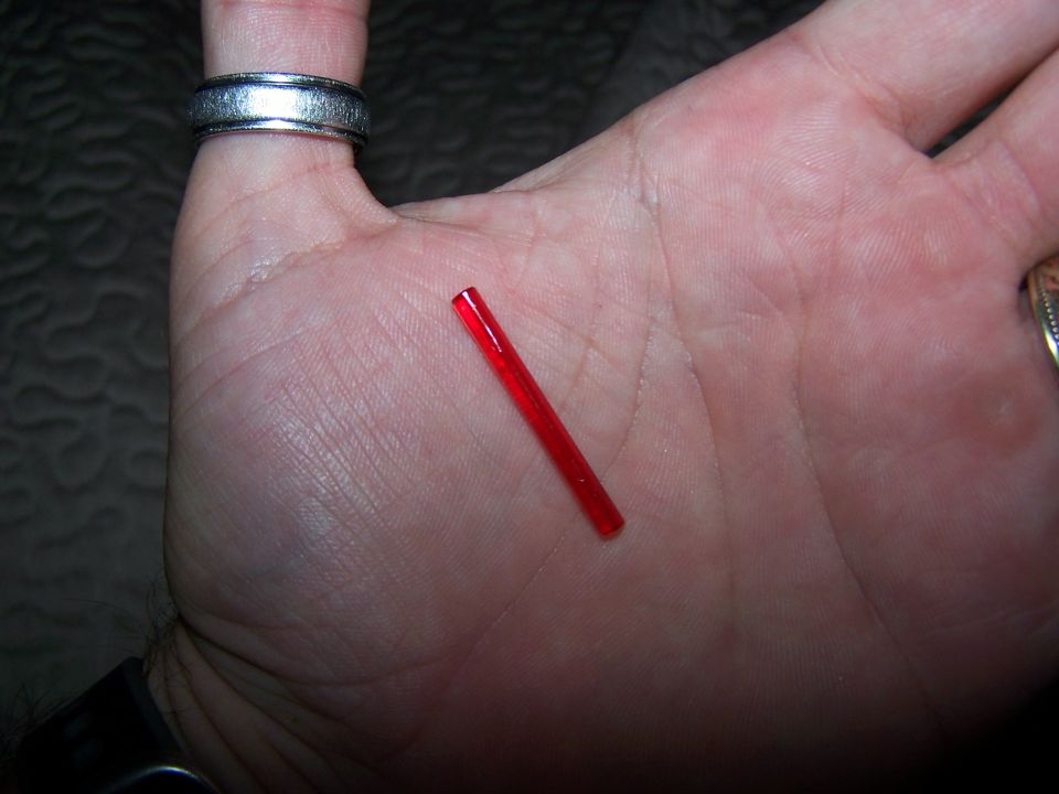Small red plastic rod held in palm with a ring on index finger