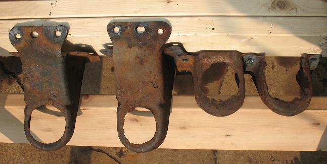 Four rusted metal brackets with holes for mounting, laid on wooden planks