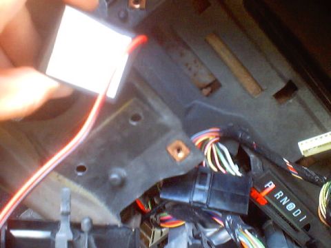 1999 Ford Taurus - A person is holding a white label near exposed wiring and the PRND1 gear selector in a vehicle's interior.