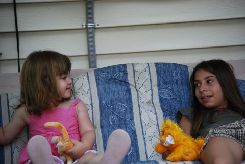 2000 Ford Crown Victoria - Two young girls sit on a couch, each holding a stuffed animal, with a light-colored wall behind them.