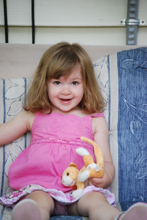 2000 Ford Crown Victoria - A young girl with blonde hair smiles while sitting on a couch and holding a stuffed cat toy.