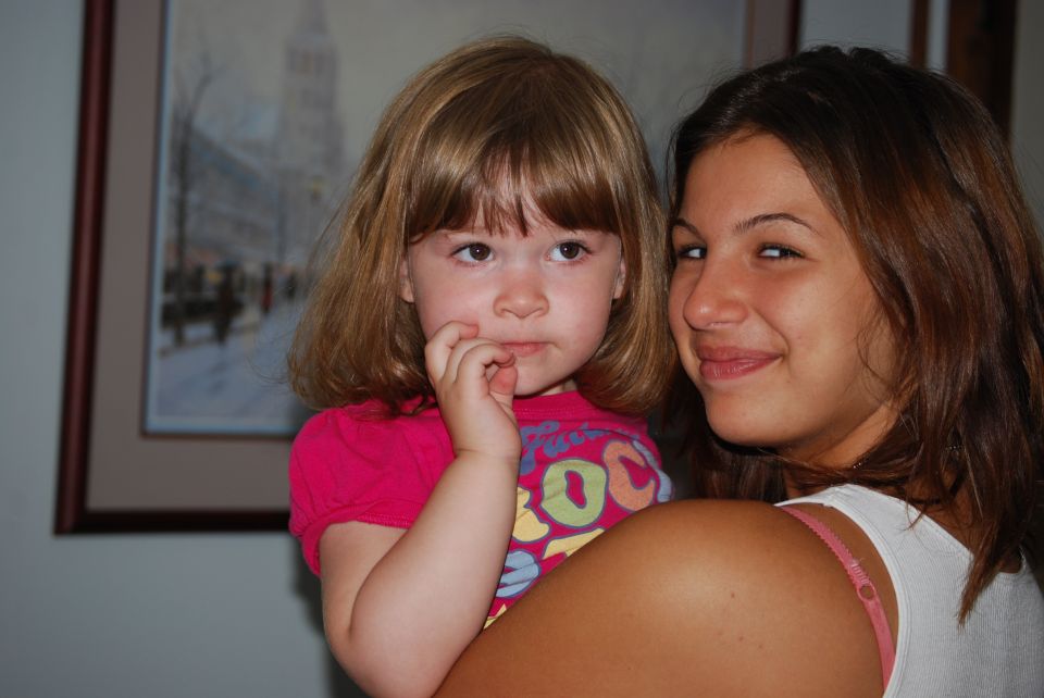 Young girl with blonde hair and a pink shirt is held by a woman with brown hair