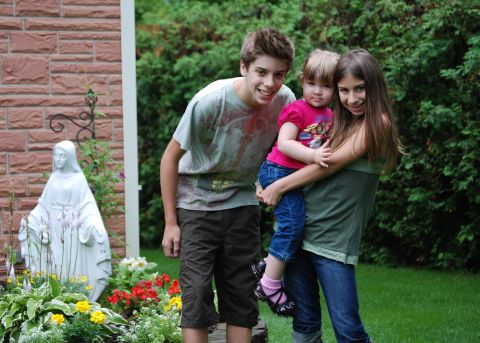 2000 Ford Crown Victoria - Three children smile for a photo in a garden setting, with a statue of Mary visible.