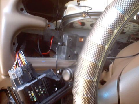 1999 Ford Taurus - Disassembled dashboard showing electrical harness plugs and connectors behind the gauge cluster, with a carbon-fiber wrapped steering wheel.