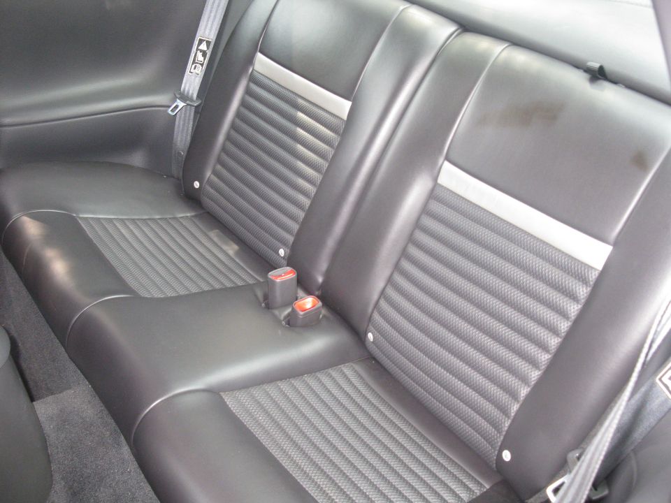 Back seat of a car with black leather seats and ribbed inserts. Seatbelts are visible