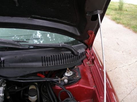 1997 Ford Taurus - View of a red car's engine bay with the hood propped open, revealing the strut tower and windshield wiper assembly.