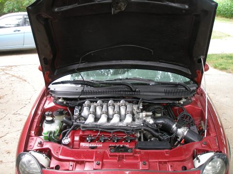 1997 Ford Taurus - The engine bay of a red car is shown with the hood open, revealing the V6 engine and various components.