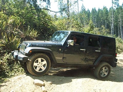 1986 Ford Bronco - A black Jeep Wrangler Rubicon is seen driving on a dirt road surrounded by trees.