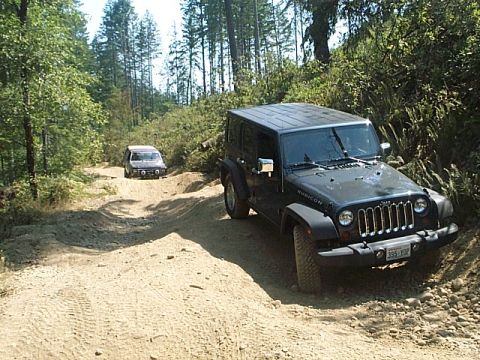 1986 Ford Bronco - Two vehicles navigate a sandy, wooded trail. The Jeep Wrangler is in the foreground.