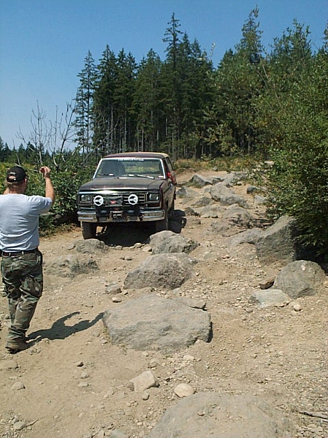1986 Ford Bronco - 1986 Ford Bronco tackling a challenging rocky path in a wooded area.
