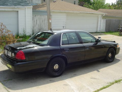 2000 Ford Crown Victoria - This black 2000 Ford Crown Victoria sedan is viewed from its rear-left quarter, parked in front of a garage.