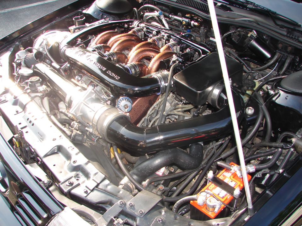 Engine bay with copper intake runners and black piping, orange battery, and "SUPERMOTORS" text