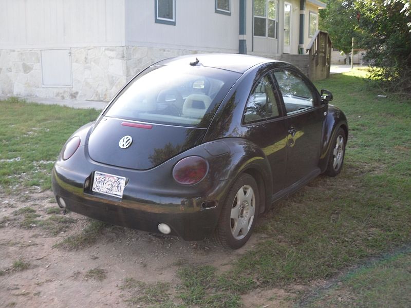 Black Volkswagen Beetle parked on dirt and grass in front of a house