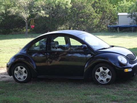 1999 Volkswagen Beetle - A black Volkswagen Beetle is parked on a grassy area with trees in the background.