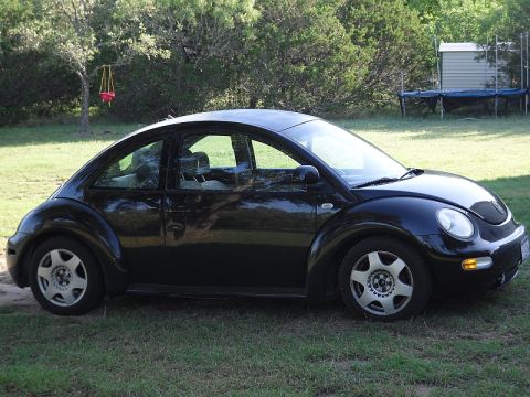 1999 Volkswagen Beetle - Side view of a black 1999 Volkswagen Beetle parked on grass.