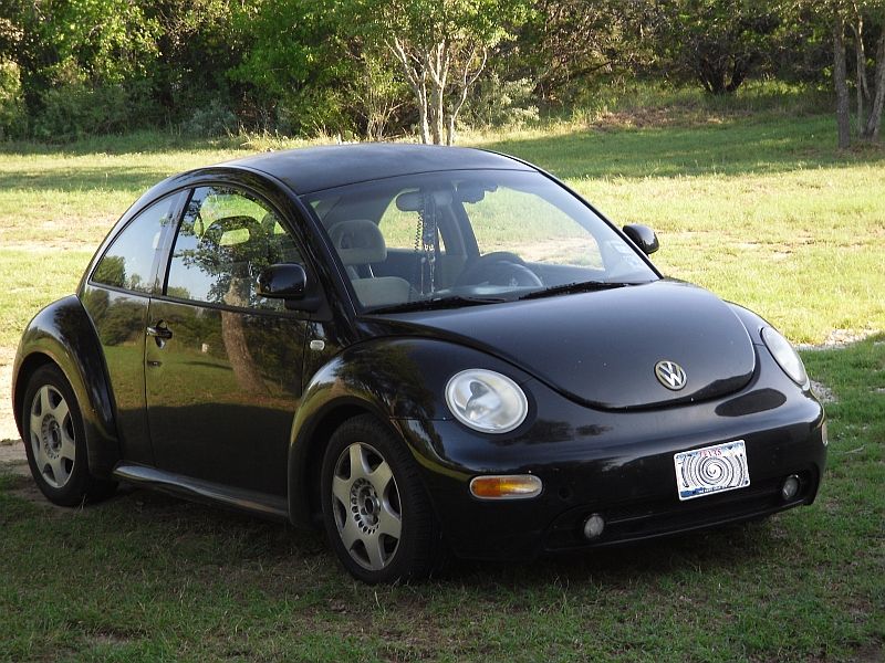 Black 1999 Volkswagen Beetle parked on grass with trees in the background