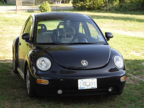 1999 Volkswagen Beetle - A black Volkswagen Beetle is parked outdoors on a grassy area with trees in the background.