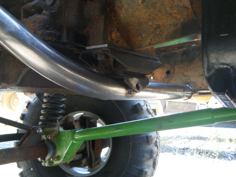 Close-up of a shiny exhaust pipe and green suspension arm on a vehicle's undercarriage