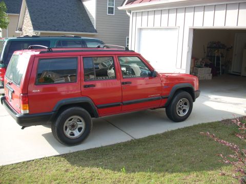 2005 Ford F-250 - A red Jeep Cherokee is parked in a driveway next to a garage, with another vehicle partially visible behind it.