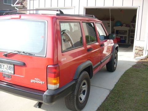 2005 Ford F-250 - A red Jeep Cherokee is parked in a driveway next to an open garage. The vehicle has a roof rack and 4x4 badging.