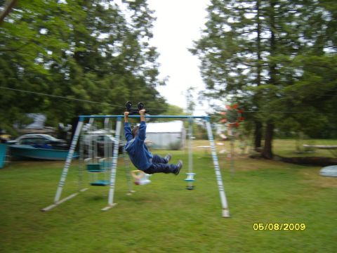 1989 Ford Bronco - A person swings on a zip line attached to a swing set in a grassy backyard.