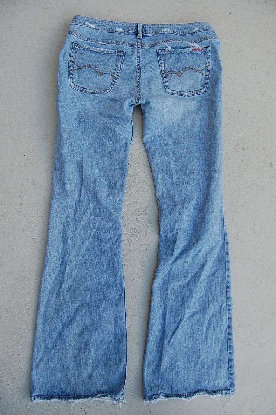 Light-wash bootcut blue jeans laid flat on concrete, back view