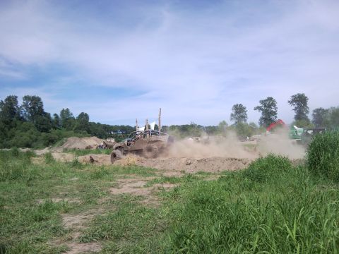 1979 Ford Bronco - An off-road buggy navigates a dusty track, with other vehicles and construction equipment visible in the background under a partly cloudy s…