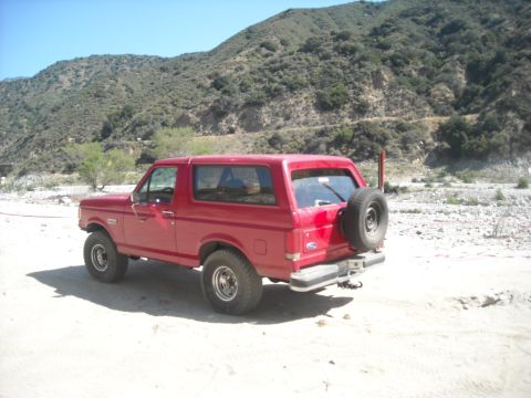 1988 Ford Bronco - This red 1988 Ford Bronco is seen in a dry riverbed, a rear-mounted spare tire and a 3/4 front view.