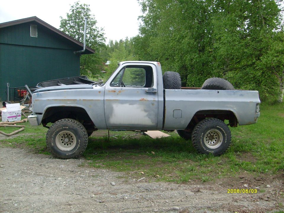 Primer-gray square-body Chevrolet 4x4 truck on mud tires, driver side profile