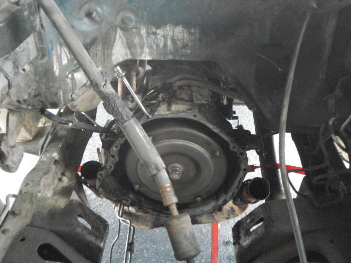 Underside view of a vehicle's transmission and driveshaft assembly, appears to be undergoing maintenance or disassembly