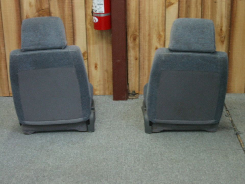 Two gray cloth bucket seats on concrete, rear view, against wood wall